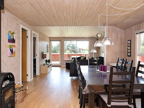 A spacious room with a wooden ceiling, a dining table with chairs, a fireplace, and a view through a large window. - 4 Star Holiday Home in Hjorring (Hjørring)