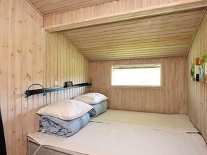 A small, wooden-paneled room with a bunk bed, a window, and a shelf with a lamp.