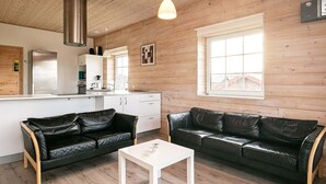 Una sala de estar moderna con dos sofás de cuero negro, una mesa de centro blanca y una zona de cocina con una campana extractora de acero inoxidable.