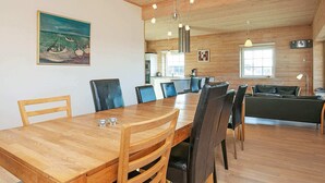 Un comedor con una mesa y sillas de madera, un cuadro en la pared y una cocina al fondo.