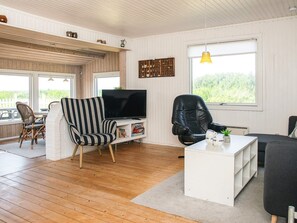 Una sala de estar amoblada con televisor, dos sillones, una mesa de centro y un ventanal con vista a zonas verdes.