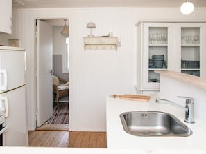 A kitchen with a stainless steel sink, a wooden countertop, and a cabinet with glassware.