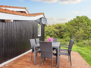 A wooden deck with a table and chairs, a satellite dish, and a view of greenery.