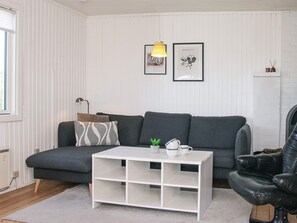 Una sala de estar moderna con un sofá gris, una mesa de centro blanca y un sillón de cuero negro. Hay dos cuadros en la pared, una lámpara y una pequeña planta sobre la mesa de centro.