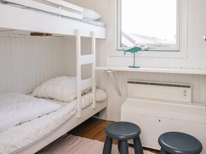 Une chambre avec un lit superposé, une fenêtre, un bureau et deux tabourets.