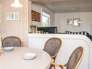 A dining area with a round table, wicker chairs, and a white brick wall. - 6 Person Holiday Home in Ringkobing (Ringkobing)