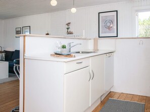 Una cocina moderna con armarios blancos, un lavamanos de acero inoxidable y una pequeña encimera. Hay objetos decorativos en la encimera y una obra de arte enmarcada sobre el lavamanos.
