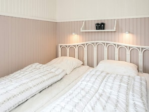A bedroom with two single beds, a white headboard, and a shelf above the beds.