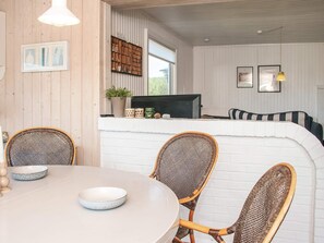 Un coin repas avec une table ronde, des chaises en osier et un mur en briques blanches.