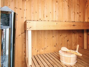 Un cuarto de sauna con un banco de madera, un balde de madera y un estante de madera.