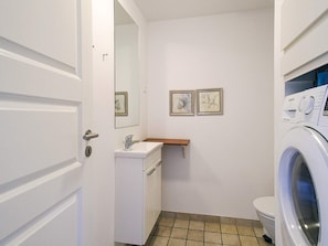 Ein kleines Badezimmer mit einem weißen Waschbecken, einer Toilette und einer Waschmaschine. An der Wand hängen zwei Bilder in Rahmen.
