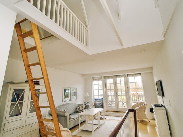 A spacious living area with a loft bedroom, a wooden ladder, a sofa, a coffee table, and a television.