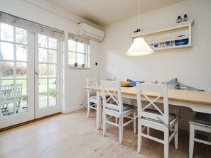Comedor con mesa de madera y sillas blancas, lámpara colgante y estante con objetos decorativos.