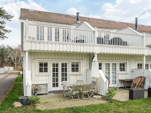 Uma casa branca de dois andares com varanda, um pátio com mobiliário de exterior e chaminé.