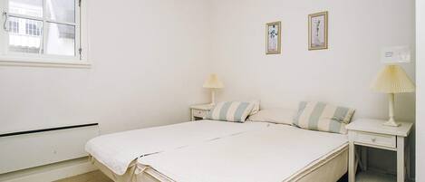 A simple, clean bedroom with a bed, two bedside tables, and a window.