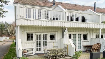 Une maison blanche à deux étages, dotée d’un balcon, d’une terrasse avec des meubles d’extérieur et d’une cheminée.