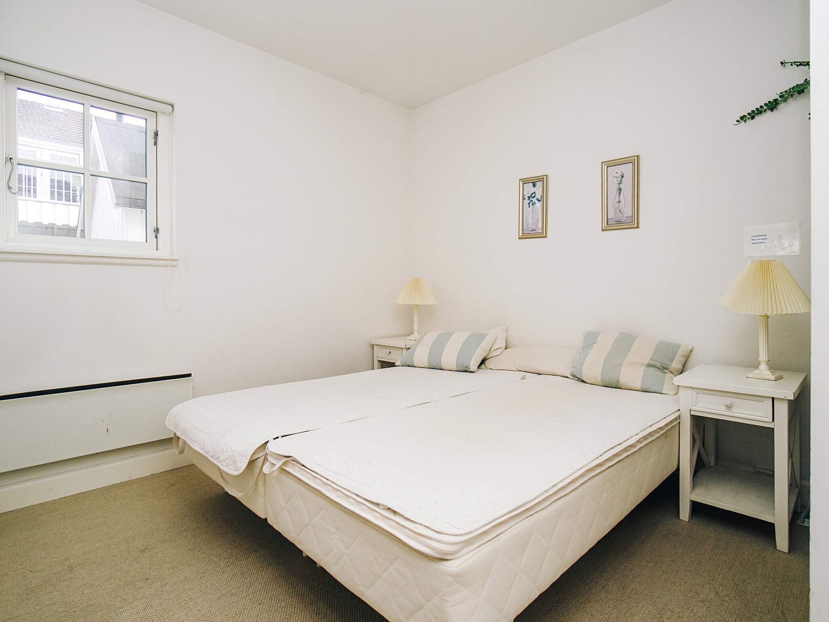 Un dormitorio sencillo y limpio con una cama, dos mesitas de noche y una ventana.
