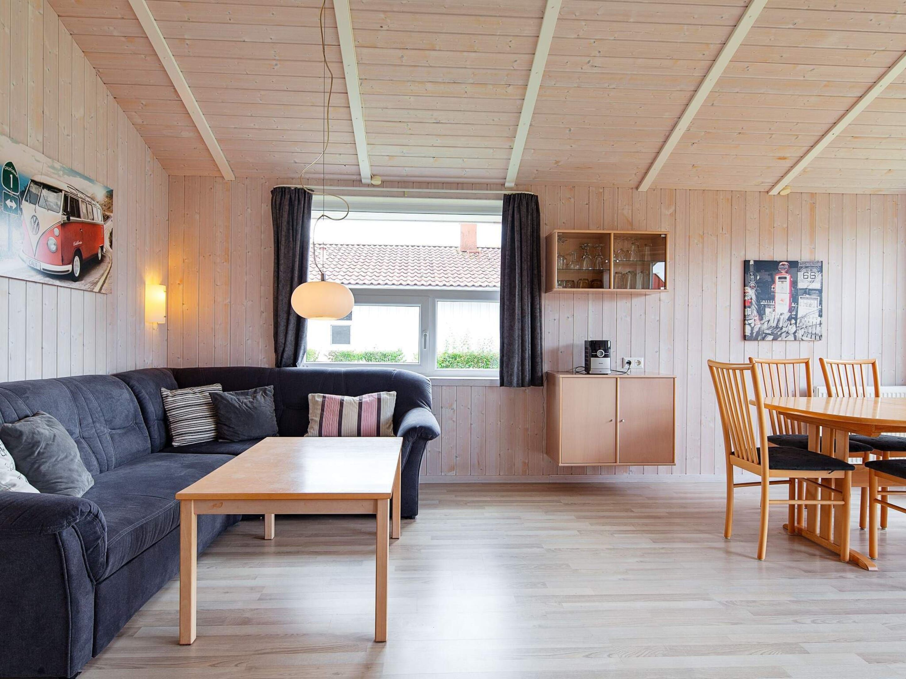 A cozy living room with a dark grey sofa, a wooden coffee table, and a dining area with wooden chairs and a table.
