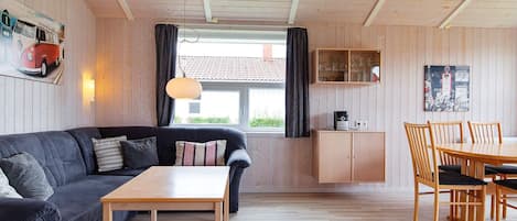 A cozy living room with a dark grey sofa, a wooden coffee table, and a dining area with wooden chairs and a table.