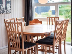 A round wooden dining table surrounded by six wooden chairs with black cushions.