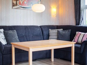 A modern living room with a dark-colored sectional sofa, a wooden coffee table, and a wall-mounted light fixture. - Holiday Home in GrÃ¶mmitz (Groemitz)