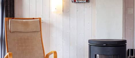 A room with a wooden chair, a black heater, and a wall-mounted light fixture.
