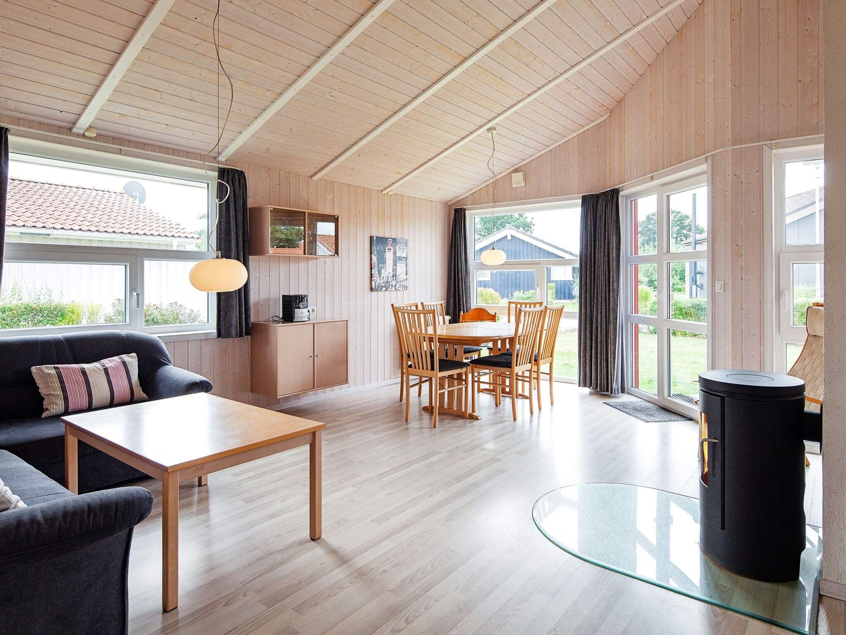 A spacious living room with a wooden ceiling, a dining area with wooden chairs, a sofa, a coffee table, and a glass-top table.