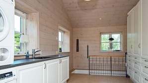 A kitchen with wooden walls, a sink, cabinets, and a window with a view of greenery. - Panoramic Retreat by Water (Borkop)