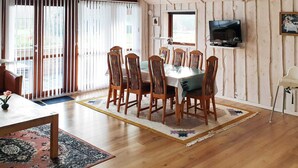 Ein Essbereich mit Holztisch und Stühlen, einem an der Wand befestigten Fernseher und Blick durch die Glastür.