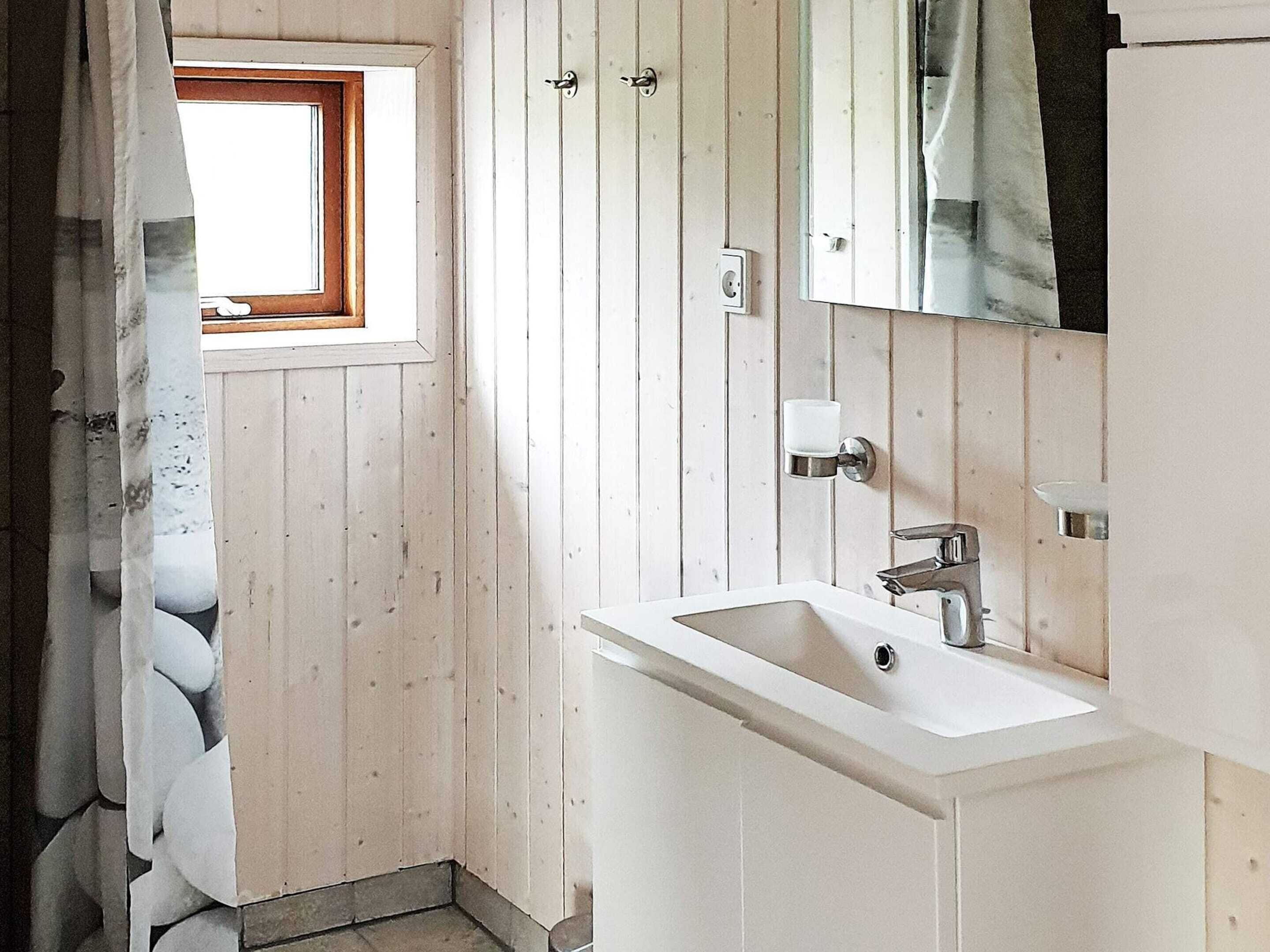 A small bathroom with a window, a sink, and a mirror.
