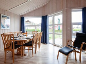 A dining area with a wooden table and chairs, large windows with curtains, and a view of the outdoors. - Holiday Home in GrÃ¶mmitz (Groemitz)