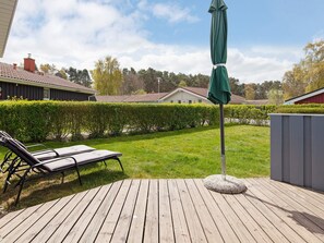 A wooden deck with a lounge chair and a green umbrella, surrounded by a well-maintained lawn and a hedge. - Holiday Home in GrÃ¶mmitz (Groemitz)