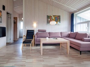 A modern living room with a wooden floor, a black leather chair, a pink sofa, and a wooden coffee table. - Holiday Home in GrÃ¶mmitz (Groemitz)