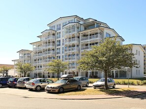 A multi-story residential building with balconies, parked cars, and trees. - Holiday Home in Grossenbrode (Grossenbrode)