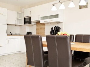 A modern kitchen with white cabinets, a wooden dining table, and black leather chairs. - Holiday Home in Grossenbrode (Grossenbrode)
