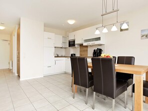 A modern kitchen with white cabinets, a microwave, and a dining area with a wooden table and black chairs. - Holiday Home in Grossenbrode (Grossenbrode)