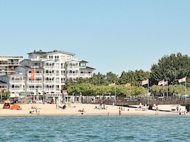 Un hotel frente a la playa con varios balcones, una playa de arena y banderas.