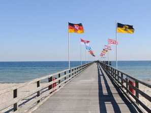 A wooden pier extending into the sea with multiple flags on poles, leading to a sandy beach. - Holiday Home in Grossenbrode (Grossenbrode)