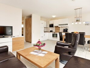A modern living room with a flat-screen TV, a wooden coffee table, and a vase of flowers. - Holiday Home in Grossenbrode (Grossenbrode)