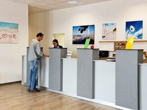 A reception area with a man and a woman behind a counter, surrounded by artwork and a wooden floor. - Holiday Home in Grossenbrode (Grossenbrode)