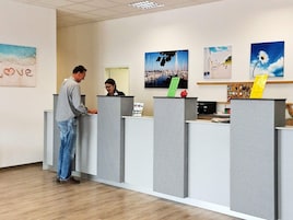 Zona de recepción con un hombre y una mujer detrás de un mostrador, rodeada de obras de arte y un suelo de madera.