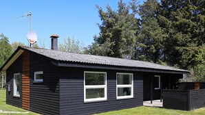 Eine kleine, eingeschossige Holzhütte mit dunkler Fassade, geneigtem Dach und einer Satellitenschüssel.