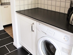A front view of a washing machine in a kitchen with a tiled backsplash and a black countertop. - Cozy Holiday Home in SÃ¦by near Sea (Sæby)