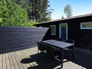 A wooden deck with a table and chairs, a wooden fence, and a building with a door and windows. - Cozy Holiday Home in SÃ¦by near Sea (Sæby)