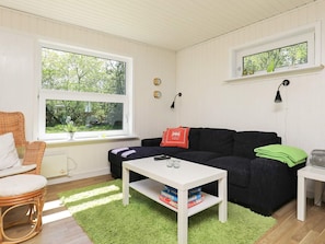 A cozy living room with a black sofa, a white coffee table, and a green rug. There are two windows providing natural light and a view of greenery outside. - Cozy Holiday Home in SÃ¦by near Sea (Sæby)