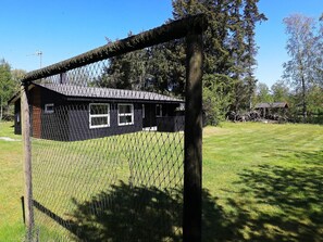 A fenced area with a building that has a dark exterior, white windows, and a sloped roof. - Cozy Holiday Home in Sæby near Sea (Sæby)