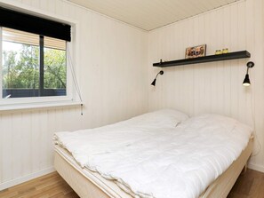 A bedroom with a bed, a window, and a shelf with decorative items. - Cozy Holiday Home in SÃ¦by near Sea (Sæby)