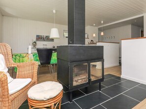 A room with a black wood-burning stove, wicker furniture, a green tablecloth, and pendant lighting.