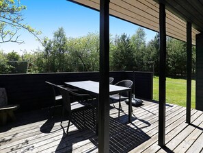 A covered outdoor patio with a table and chairs, surrounded by a wooden deck and a view of trees and a fence. - Cozy Holiday Home in SÃ¦by near Sea (Sæby)