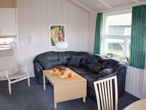A living room with a dark leather sofa, a wooden coffee table, a white armchair, and a painting on the wall. - Holiday Home in Otterndorf (Otterndorf)